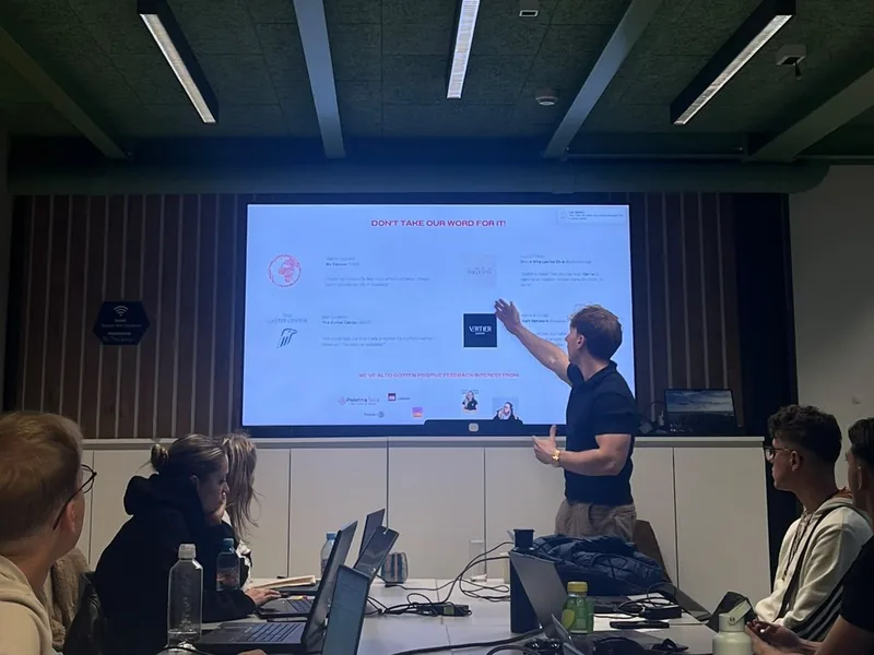 A lecturer points to a slide at an AI workshop at Impact Hub Ljubljana while participants follow at their laptops
