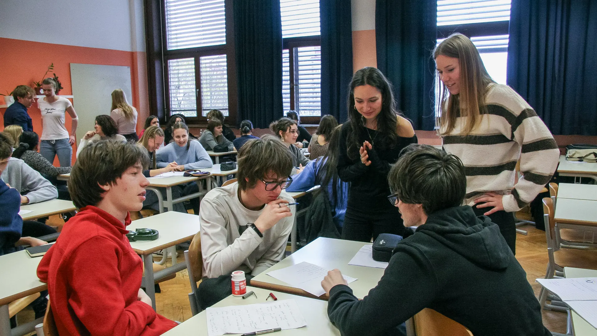 A secondary-school classroom in discussion: students talk a question through across their desks, with the rest of the class at work behind them