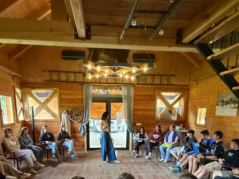 Entrepreneurship school participants sitting in a wide circle in a timber hall while a young woman speaks in the middle