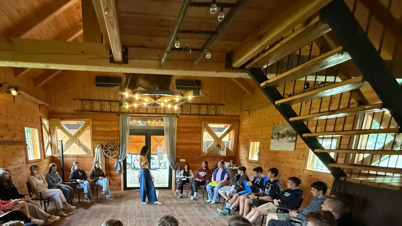 Entrepreneurship school participants sitting in a wide circle in a timber hall while a young woman speaks in the middle