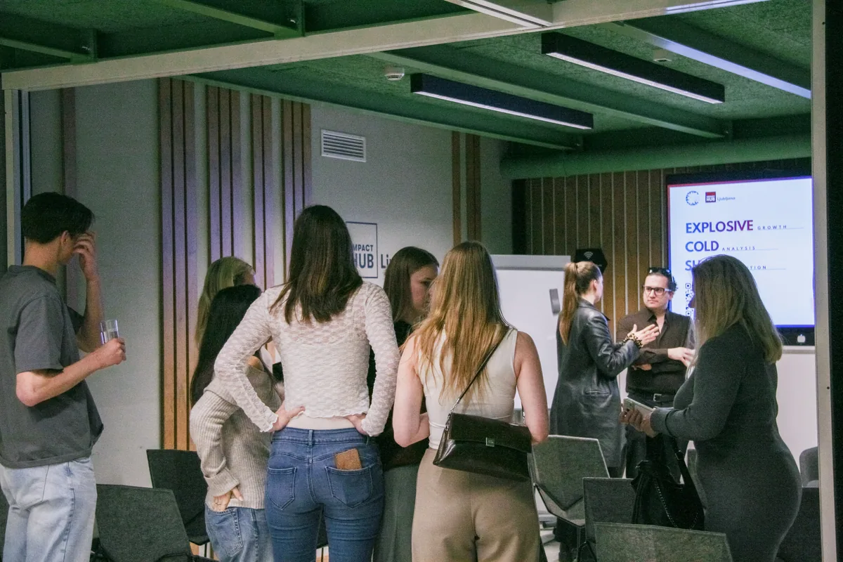 Visitors standing in small groups after the talk at Impact Hub Ljubljana, drinks in hand, the title slide still on the screen behind them