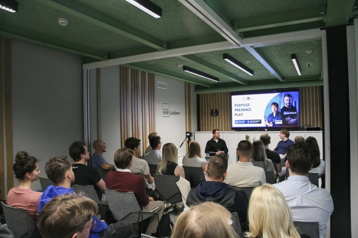 The full event room at Impact Hub Ljubljana seen from the back row, the audience facing the stage where Klemen Selakovič and moderator Marko Grad sit under the “Purpose. Presence. Play.” slide